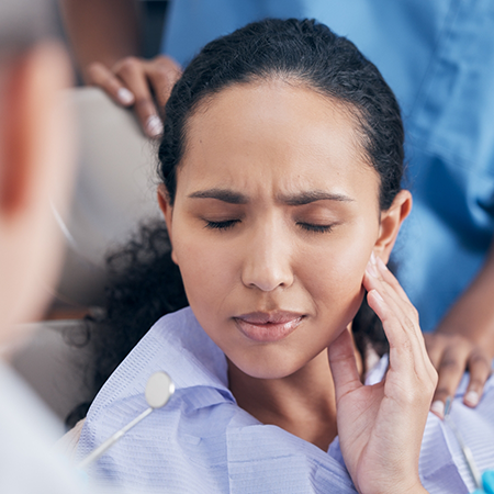Woman holding her cheek in pain while seeing her emergency dentist in Deerfield