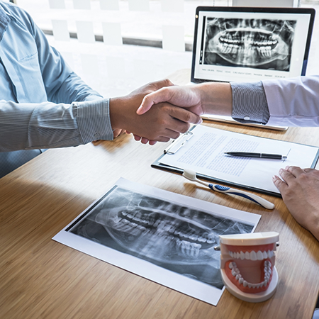 Person shaking hands with their dentist across a desk