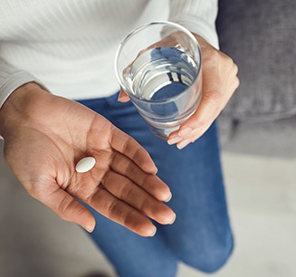 Man in grey shirt holding glass of water and a pill