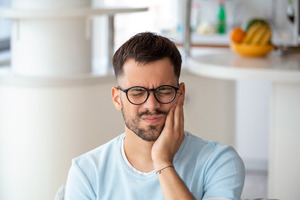 Man with glasses rubbing jaw in pain